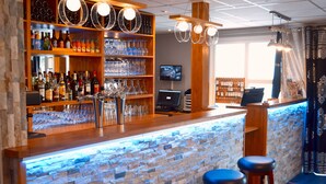 A bar area with a stone wall, shelves with bottles and glasses, a TV, and bar stools. - Fasthôtel Orléans Sud Zénith (Orléans)
