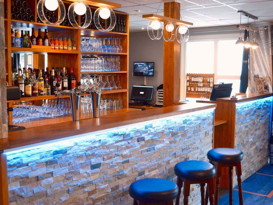 A bar area with a stone wall, shelves with bottles and glasses, a TV, and bar stools.