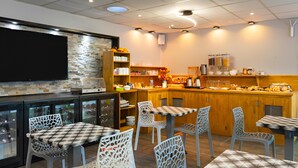 A restaurant with a bar area, seating with patterned chairs, a stone wall, and a kitchen in the background. - Fasthôtel Orléans Sud Zénith (Orléans)