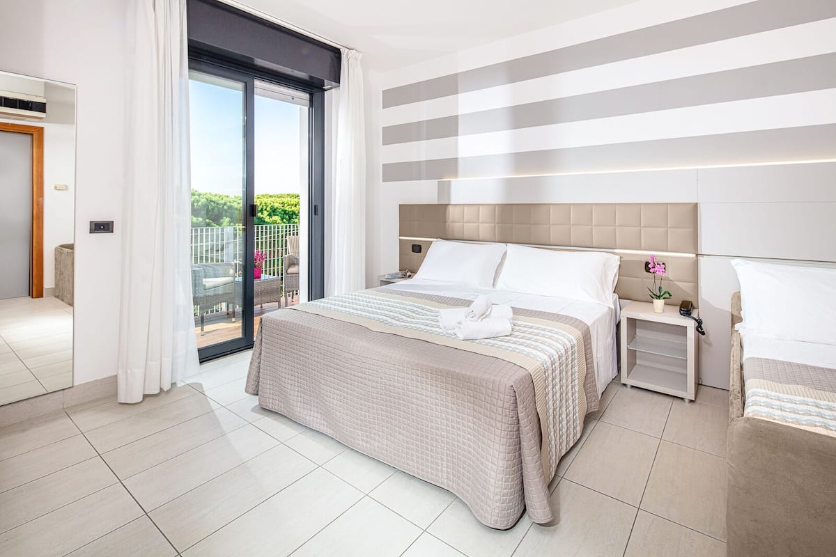 A modern hotel bedroom with a large bed, a nightstand, a view of the outdoors, and a sliding glass door to a balcony.