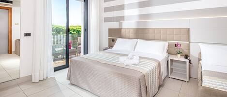 Une chambre d’hôtel moderne avec un grand lit, une table de chevet, une vue sur l’extérieur et une porte-fenêtre coulissante donnant sur un balcon.