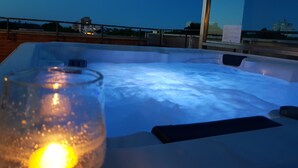 A hot tub with a glass and candle, a wooden deck, and a view of buildings in the background. - Hotel Helvetia (Lignano Sabbiadoro)