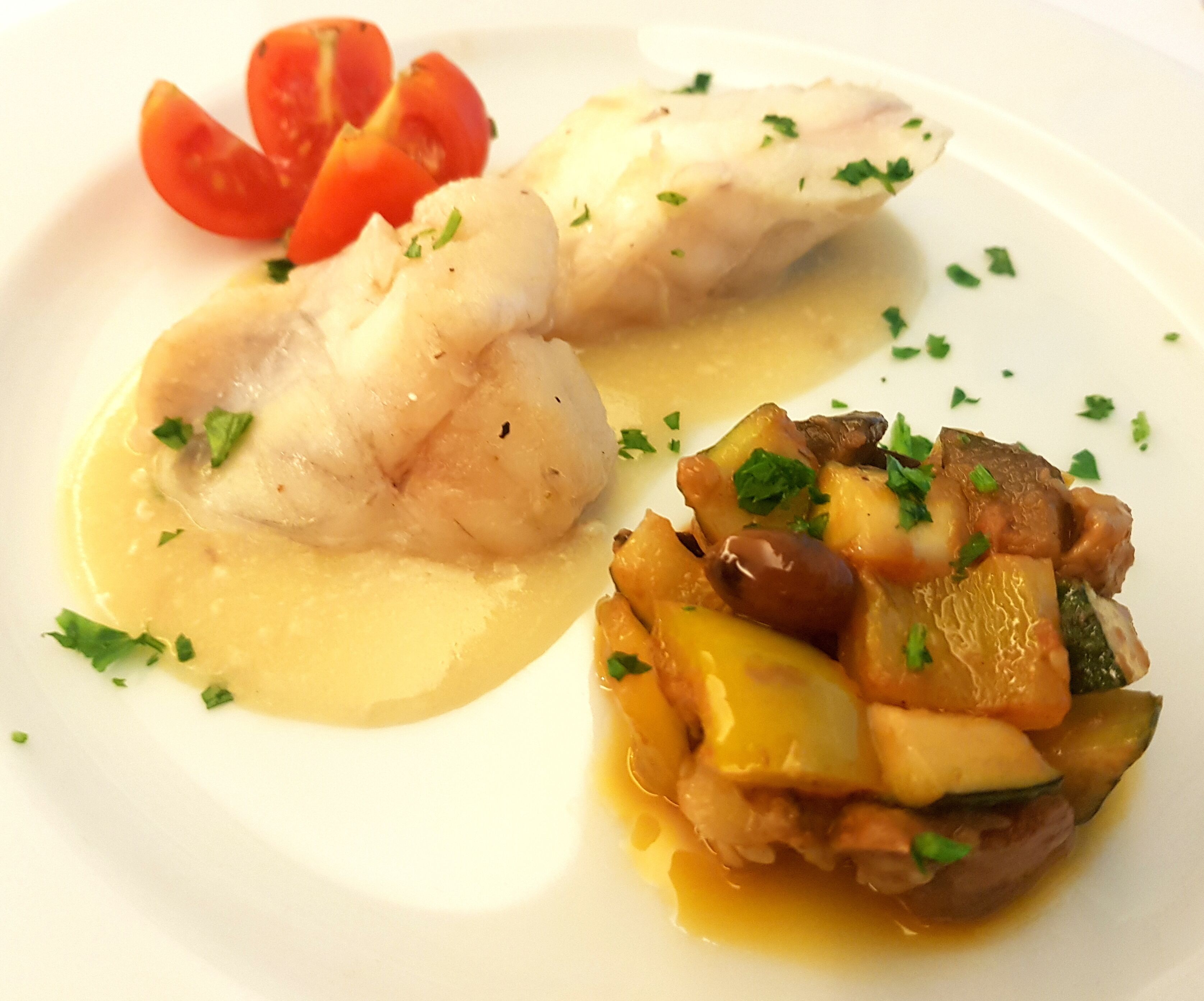 A plate with fish fillets, a vegetable medley, and cherry tomatoes.