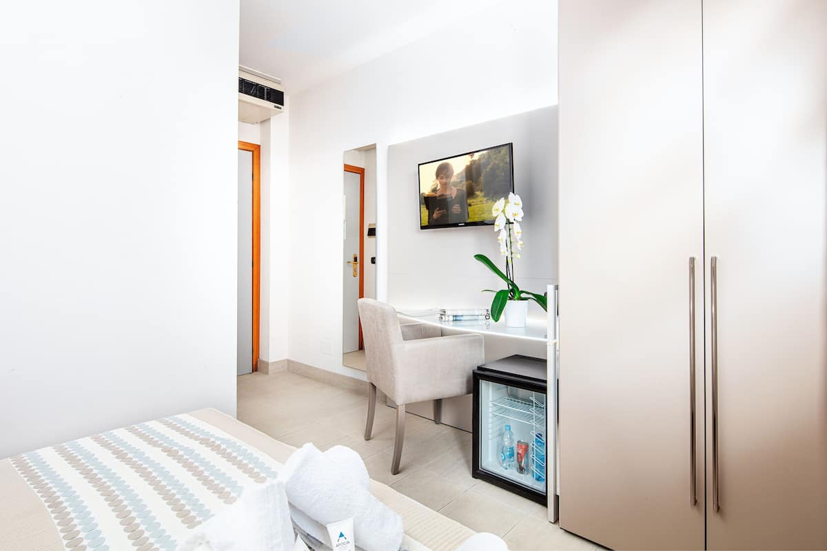 A modern hotel room with a bed, a desk, a chair, a refrigerator, and a TV mounted on the wall.