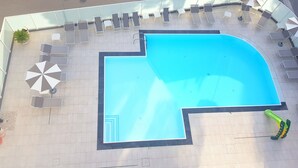 An outdoor swimming pool with a corner design, surrounded by lounge chairs and umbrellas. - Hotel Helvetia (Lignano Sabbiadoro)
