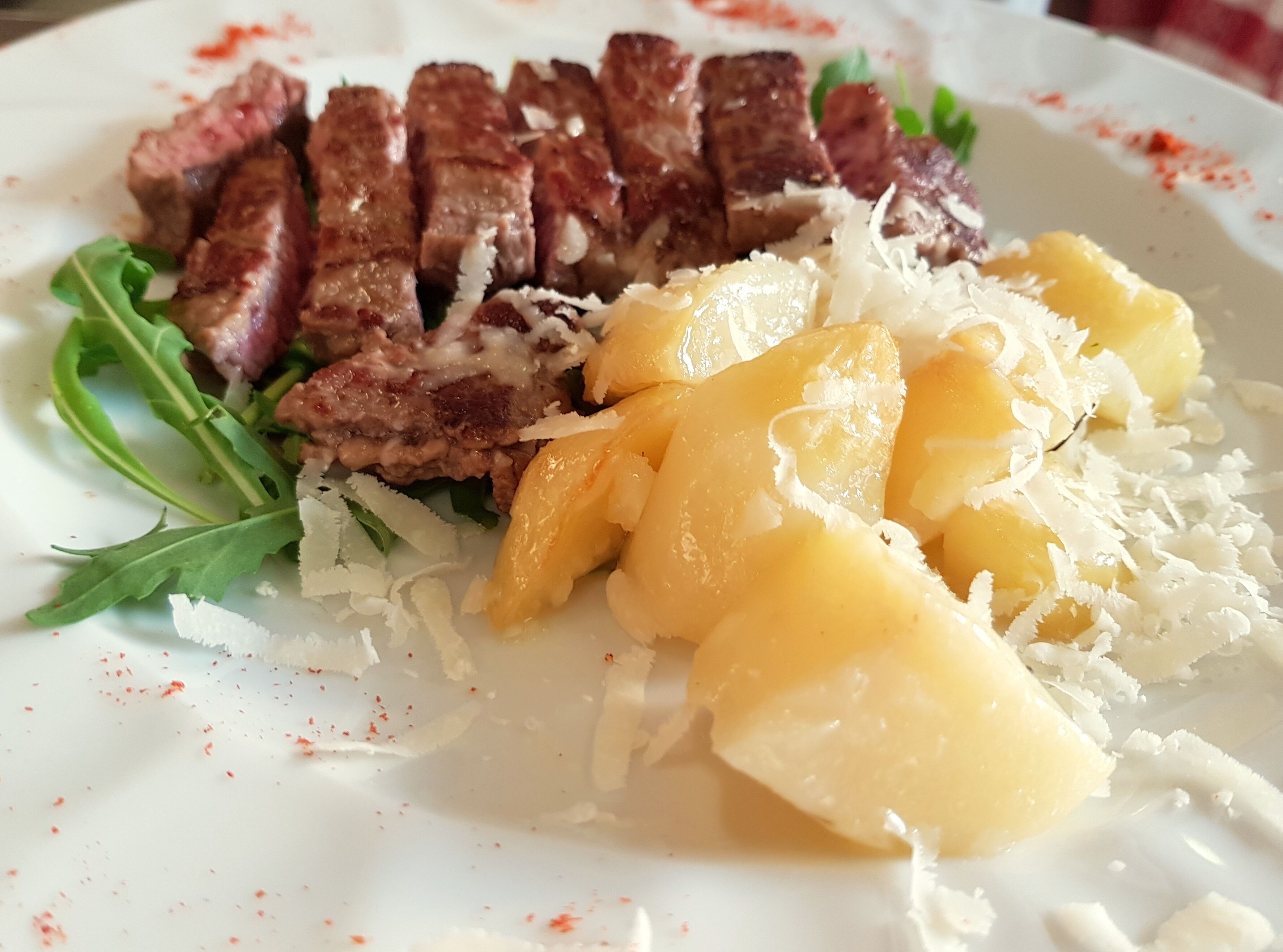 A plate with sliced steak, mango chunks, shredded cheese, and arugula.