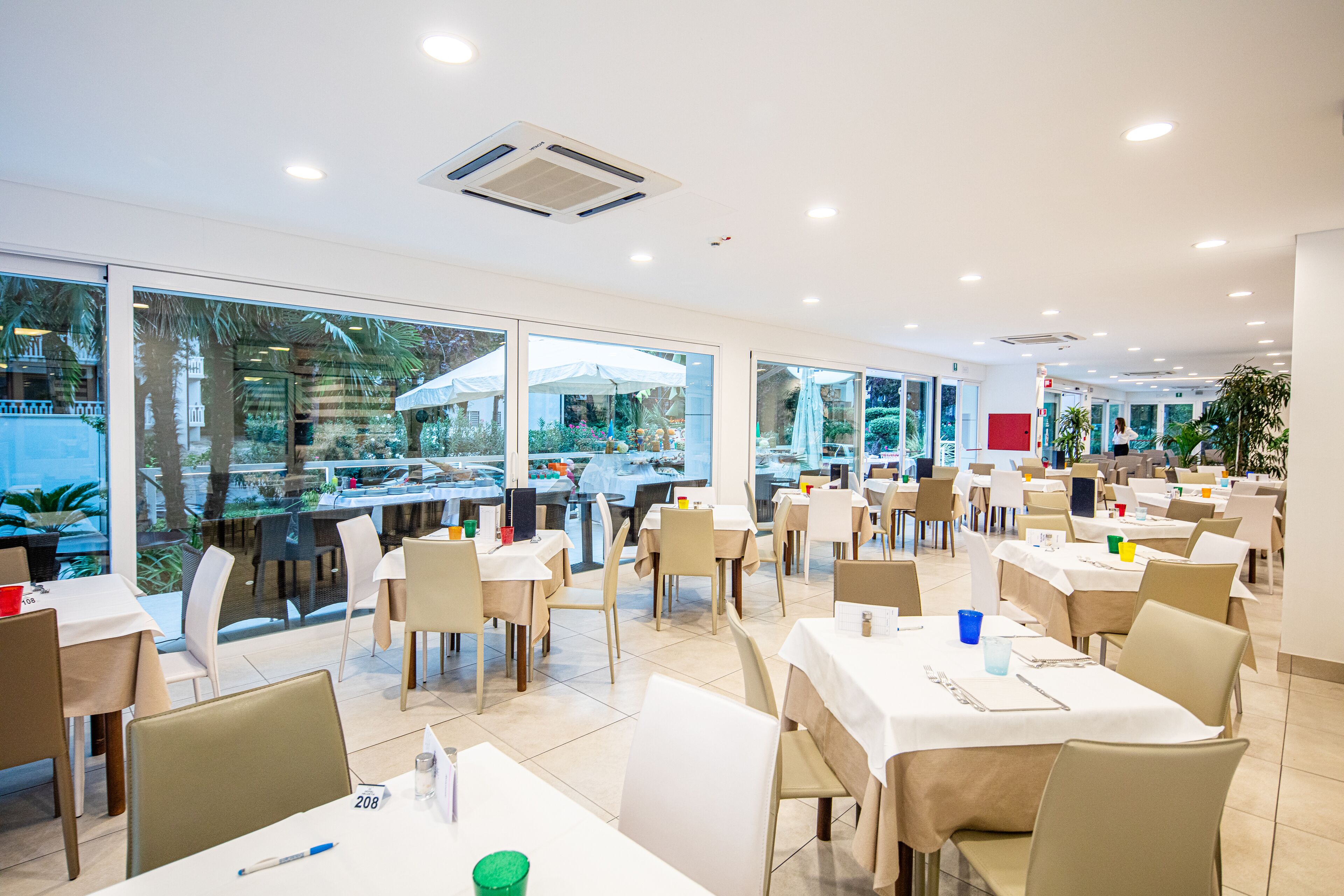 Ein geräumiges Restaurant mit mehreren Tischen und Stühlen, großen Fenstern mit Blick ins Freie und einem modernen, stilvollen Interieur.