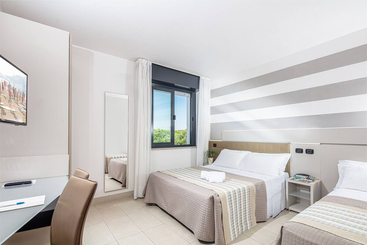 A hotel room with two beds, a desk, a chair, a TV, and a window with curtains.