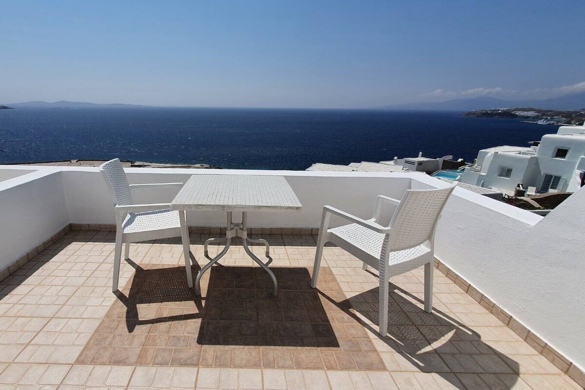 A terrace with a table and chairs, overlooking a sea view.