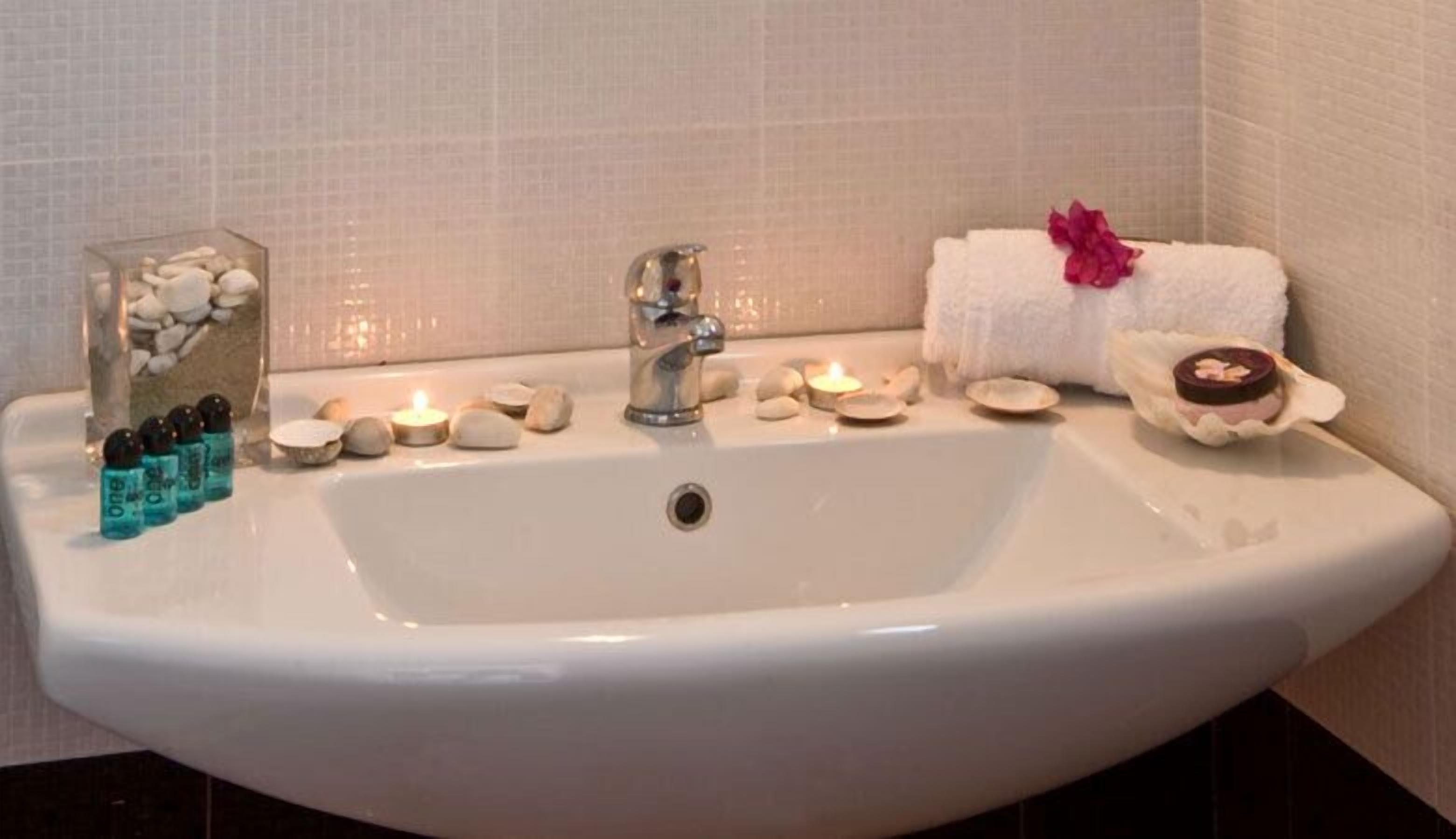 A bathroom sink with a glass container of bath salts, a lit candle, and a small tray with a candle and a bath bomb.