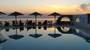 A poolside area with lounge chairs and umbrellas, a stone archway, and a sunset view. - Gorgona Hotel (Mykonos)