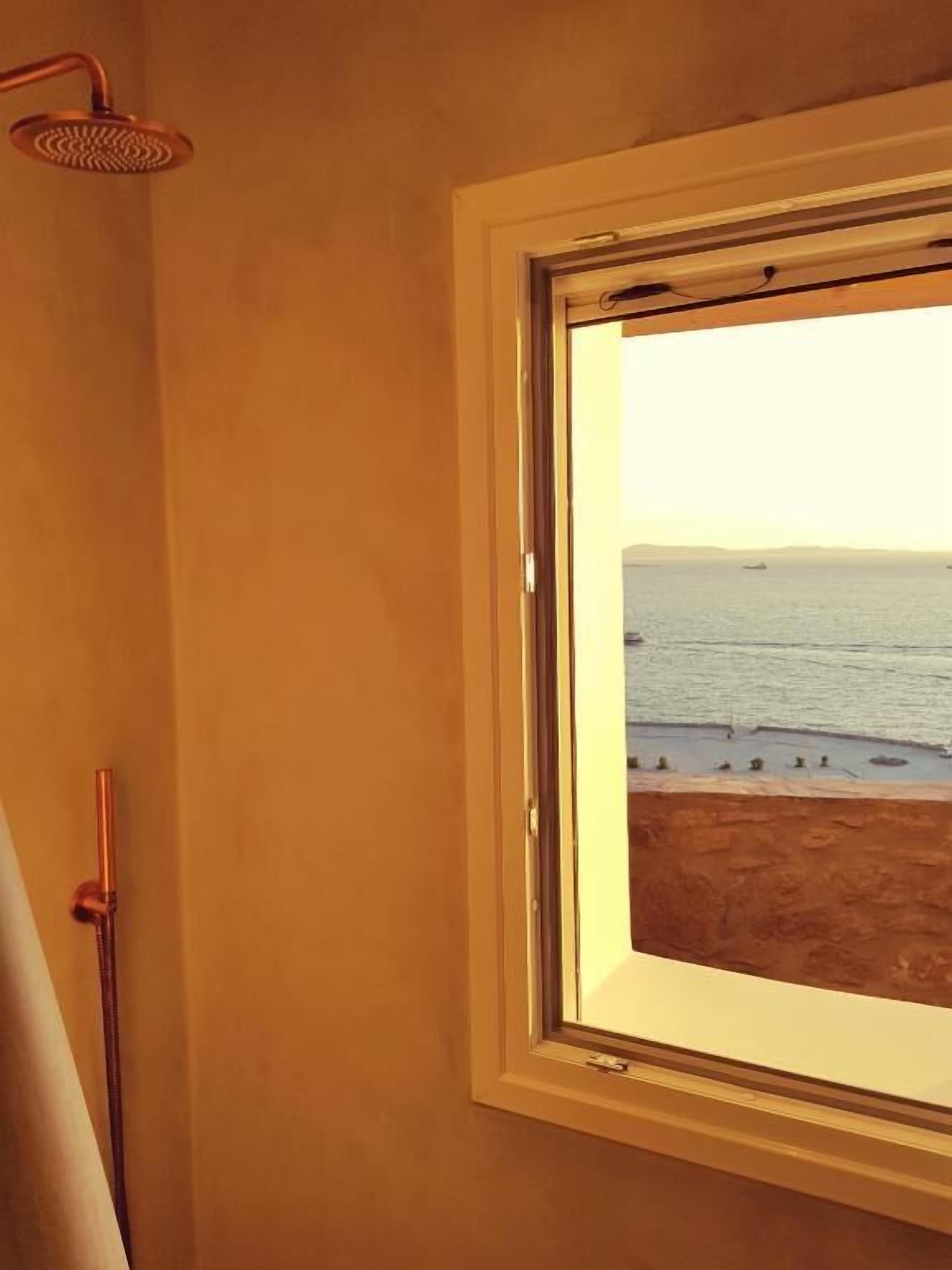A bathroom with a shower, a window with a view of the beach, and a wooden door.