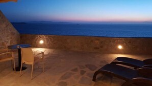 An outdoor seating area with a view of the sea, stone walls, and wooden ceiling. - Gorgona Hotel (Mykonos)