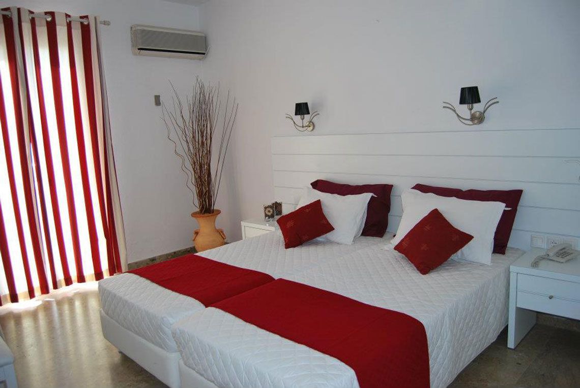 A double bed with red and white bedding, a bedside table with a lamp, and a potted plant.