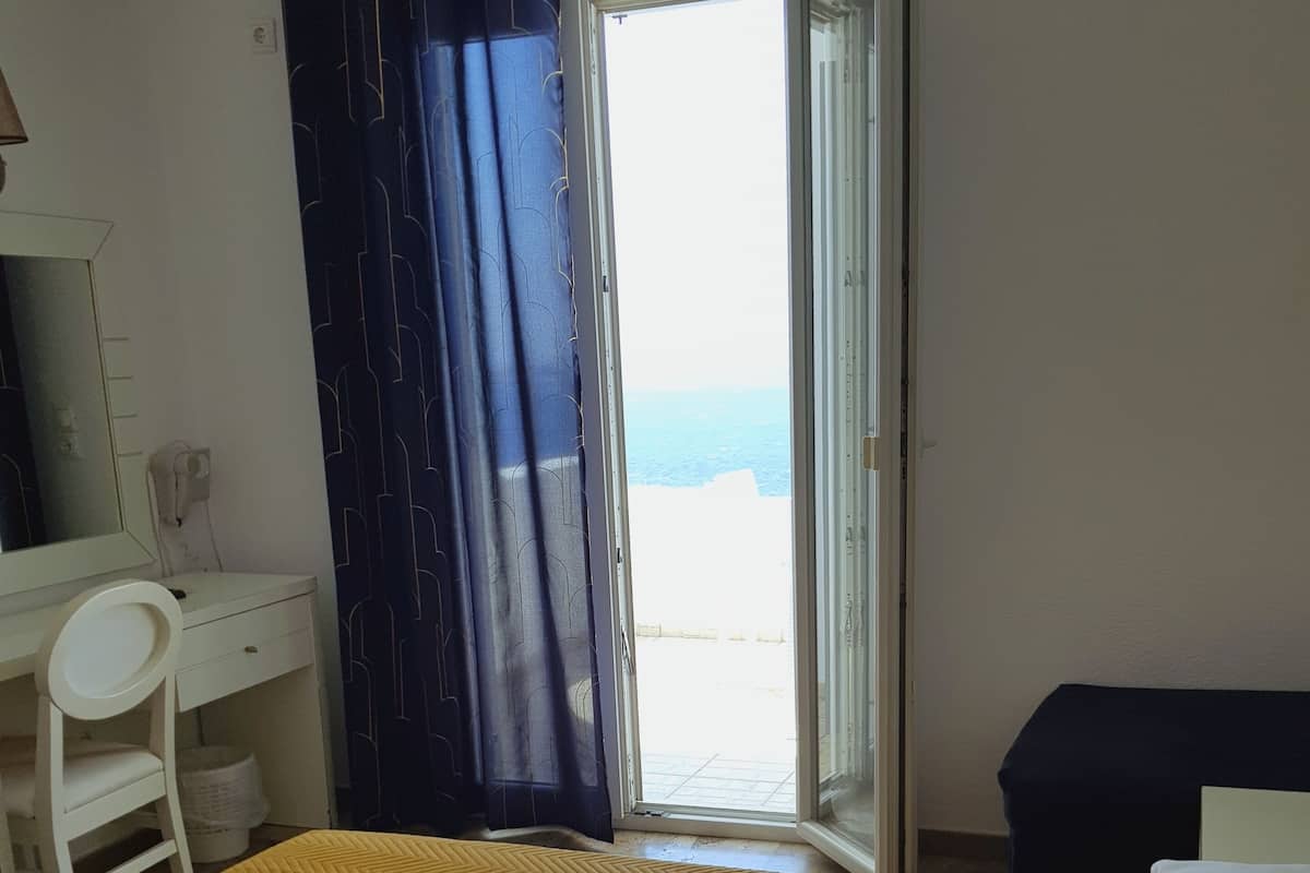 A hotel room with a bed, a desk, and a view of the sea.