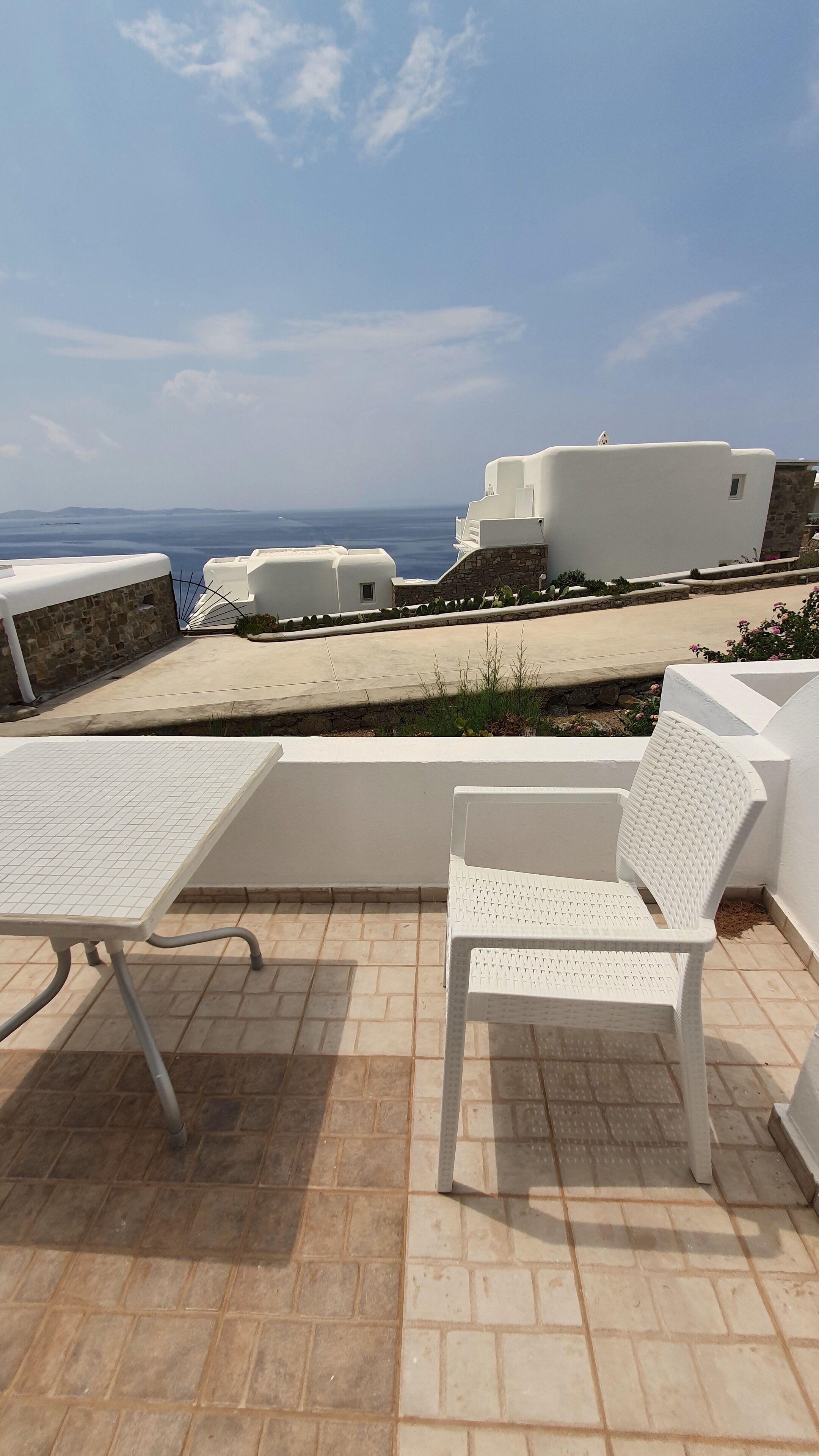 Una terraza con mobiliario exterior blanco, vista al mar y un muro de piedra.