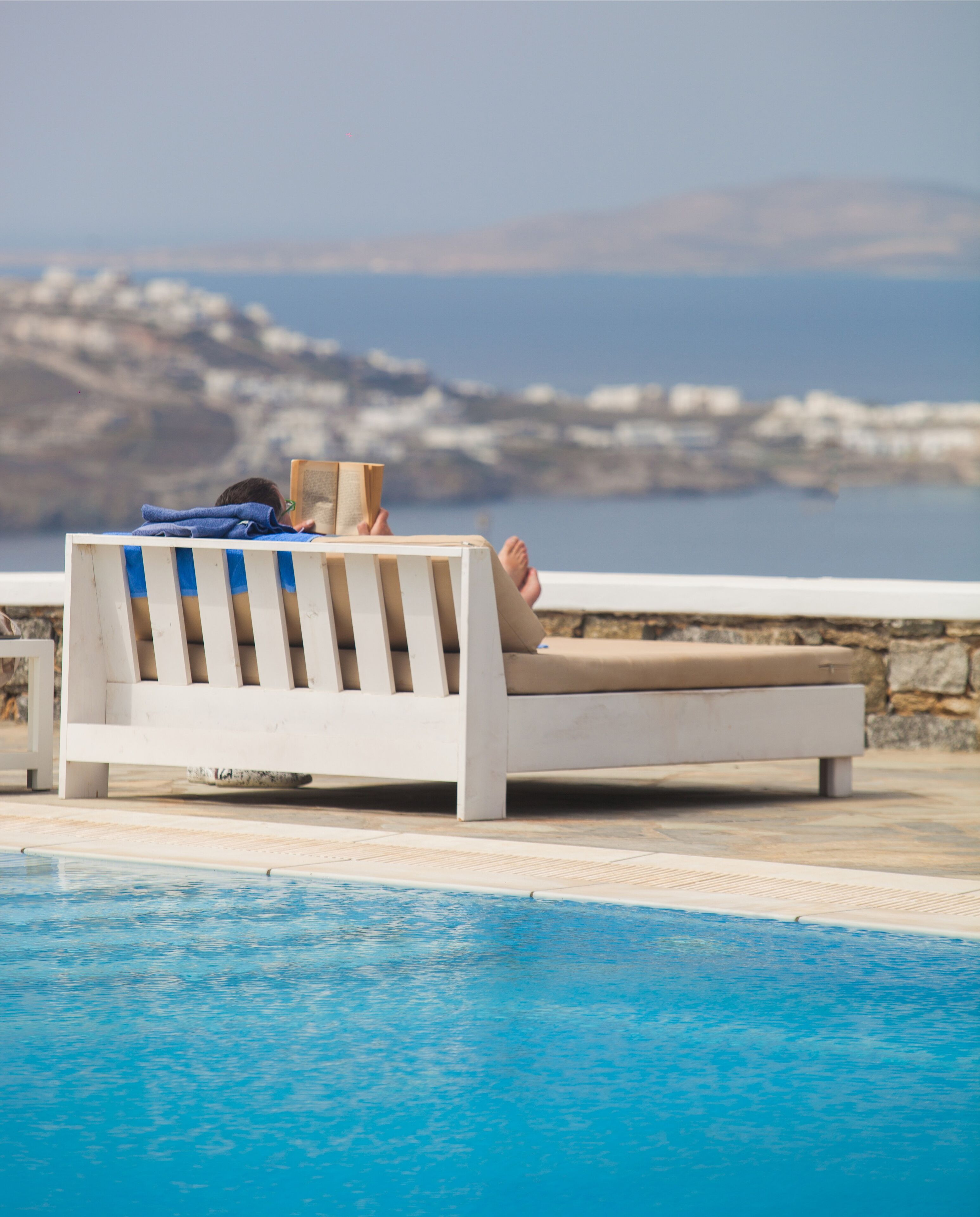 A poolside lounge chair with a person reclining, a towel, and a book.