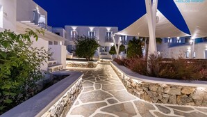 Een modern resort met een pad van stenen dat leidt naar een zwembad, omringd door witte gebouwen met balkons.