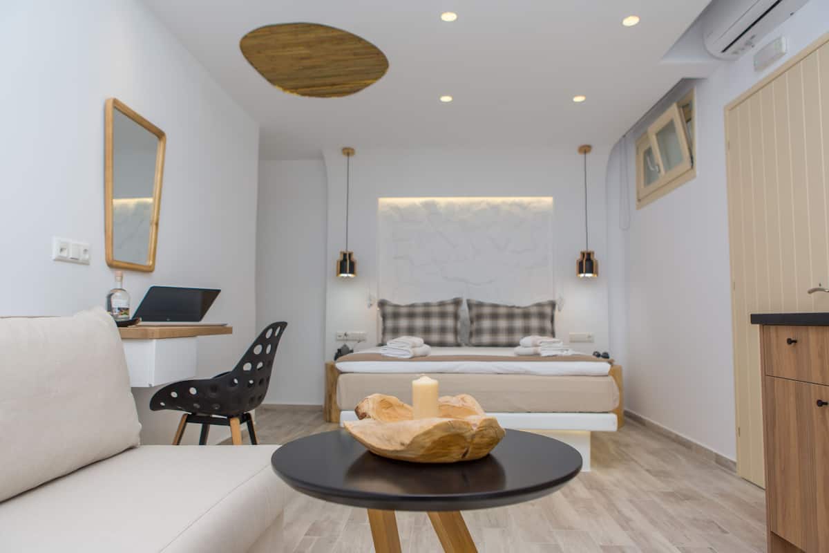 A modern bedroom with a bed, a desk with a laptop, a chair, and a small round table with a candle.