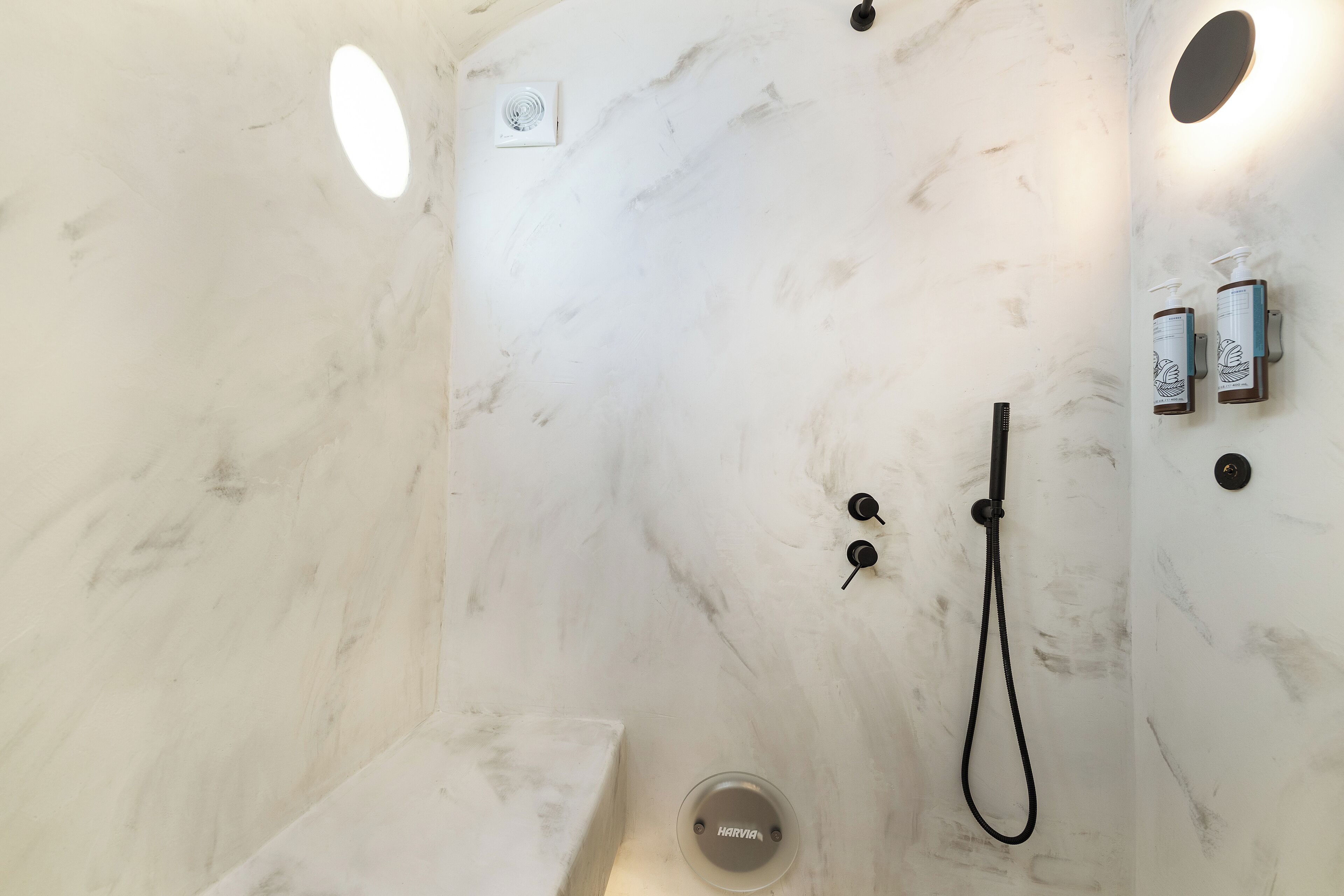 A bathroom with a marble wall, a handheld showerhead, and two wall-mounted hand soap dispensers.