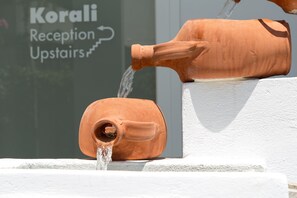Een terracotta waterornament met stromend water van een grotere naar een kleinere container, geplaatst op een witte rand.