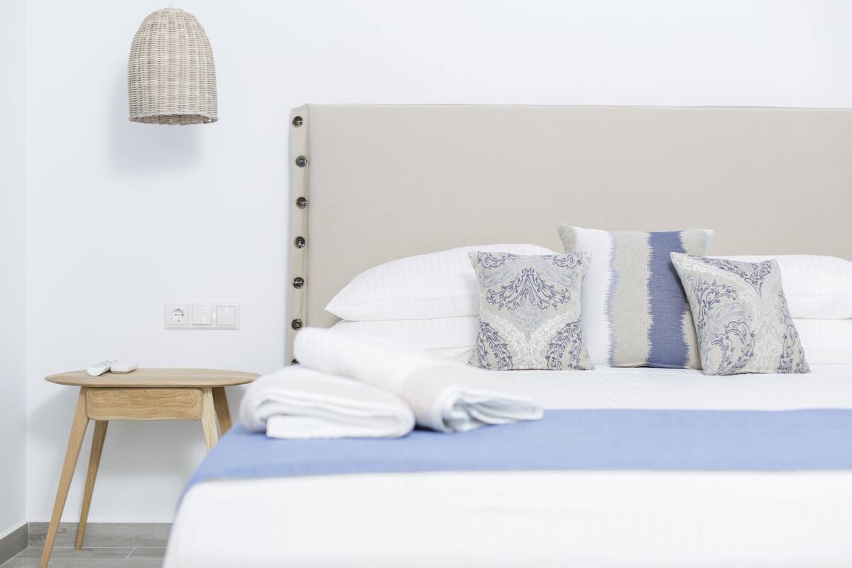 A neatly made bed with white and blue patterned pillows, a blue bedspread, and a small wooden side table with a white lamp.
