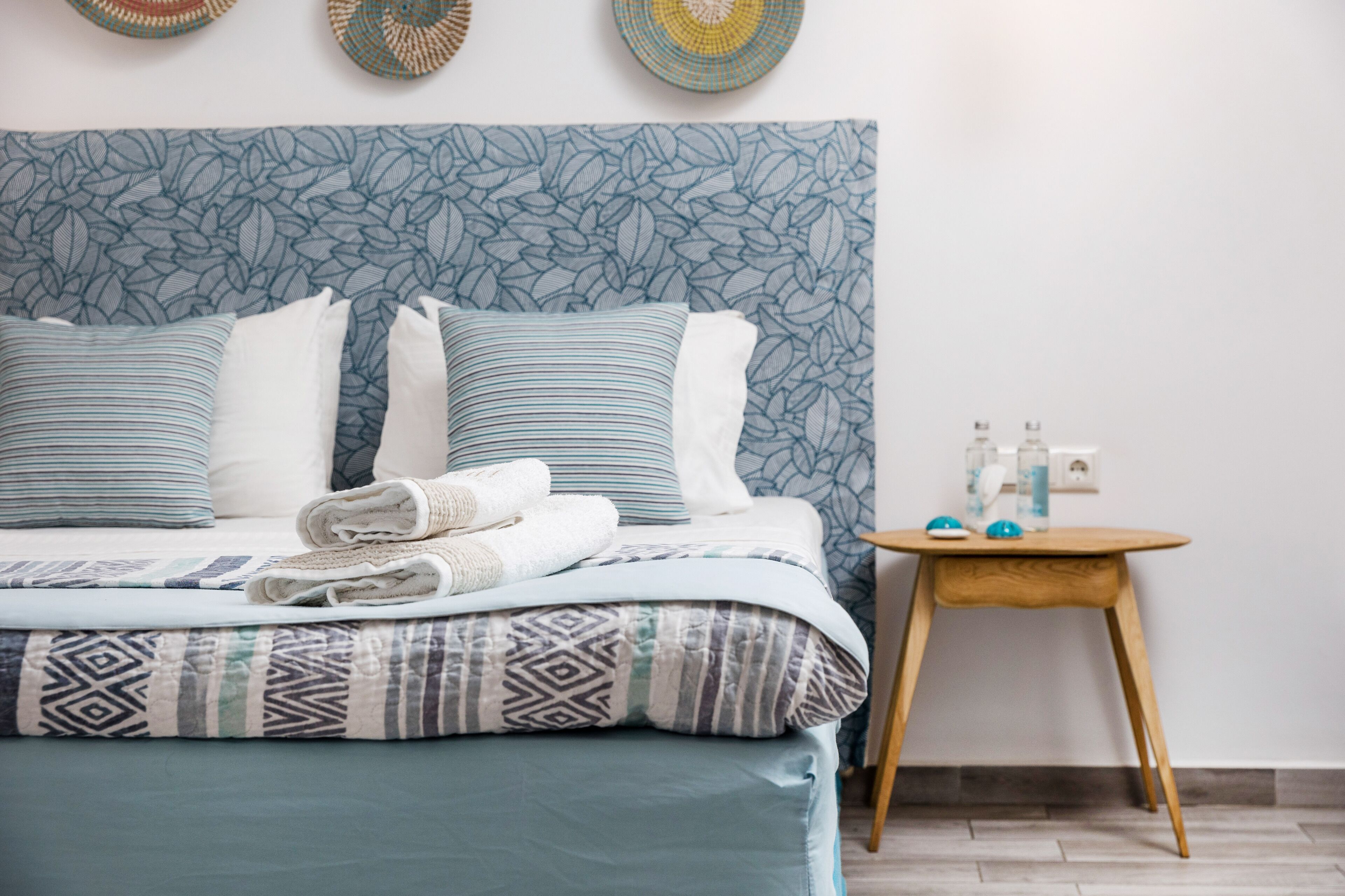A neatly made bed with patterned bedding, a bedside table with toiletries, and a wall with a leaf-patterned headboard.