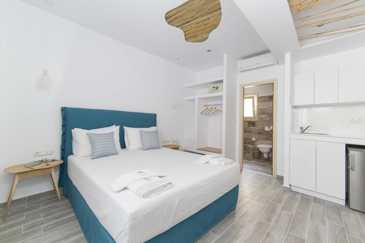 A modern bedroom with a large bed, bedside tables, a wardrobe, and a kitchenette.
