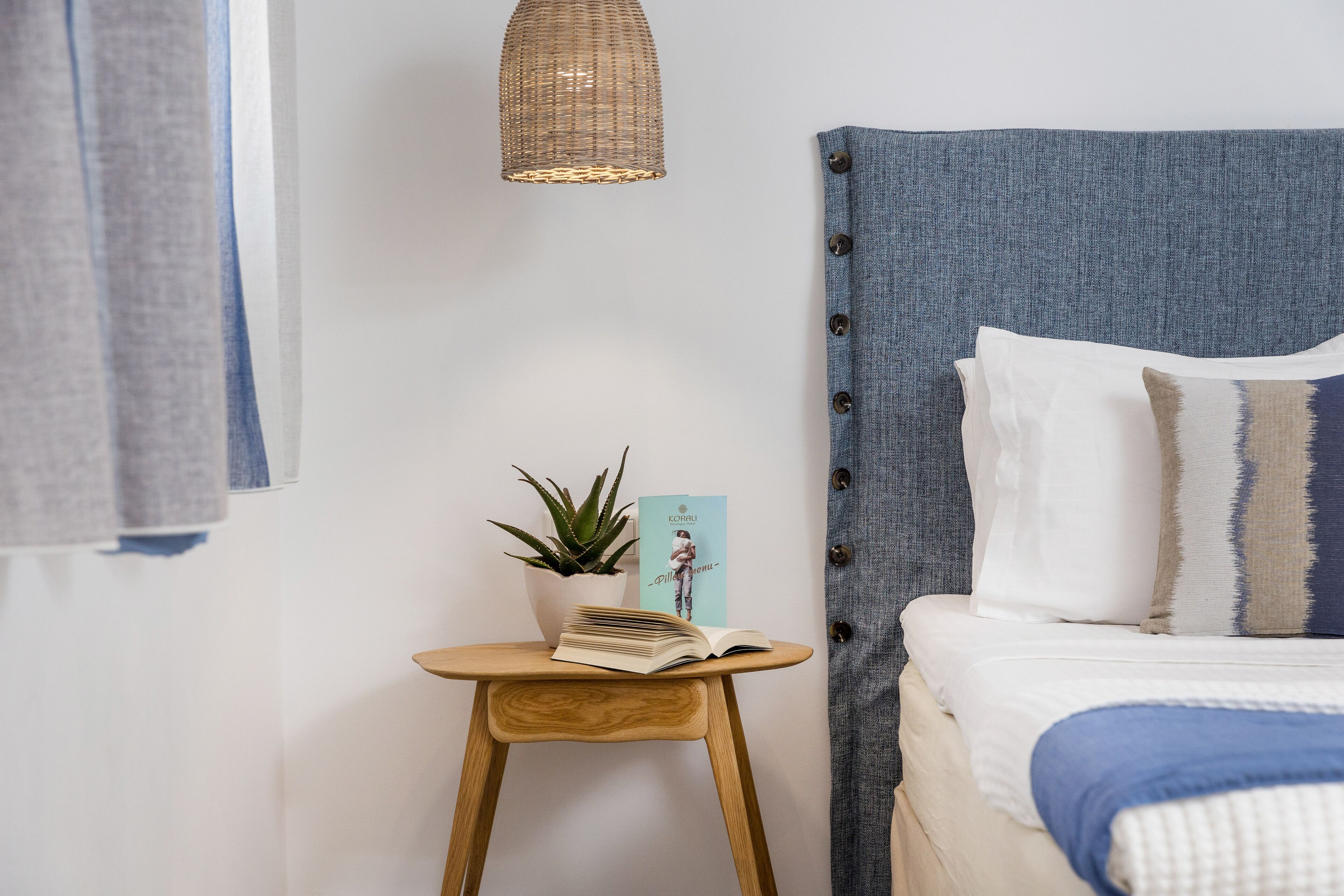 A neatly arranged bedroom with a bed, a small wooden side table, a potted plant, and a hanging light fixture.