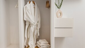 Un dressing où l’on peut entrer, avec une robe suspendue, des serviettes pliées et un vase avec des plantes vertes posé sur une étagère.