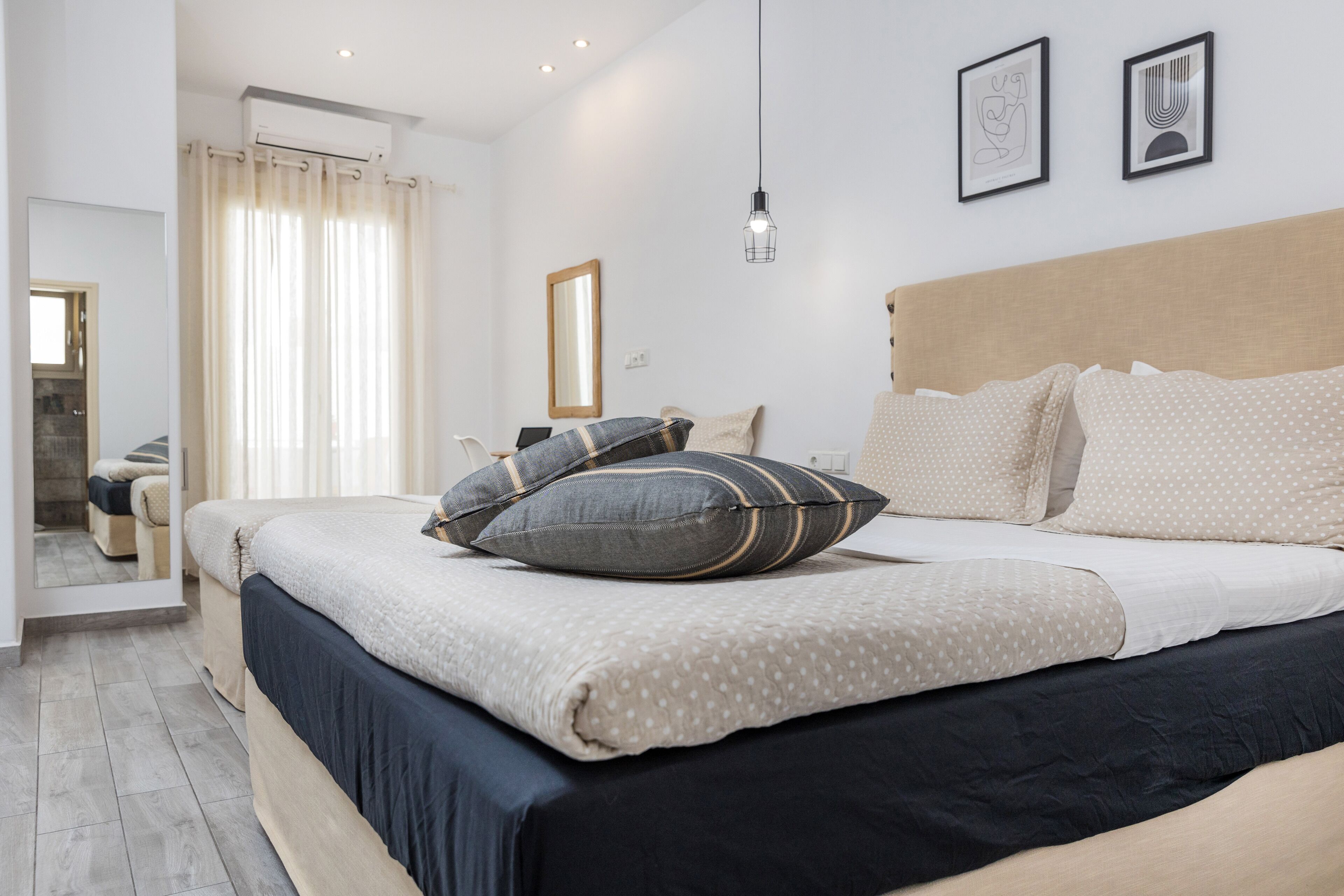 Een slaapkamer met een bed, kussens, een hoofdbord, een spiegel en een hanglamp.