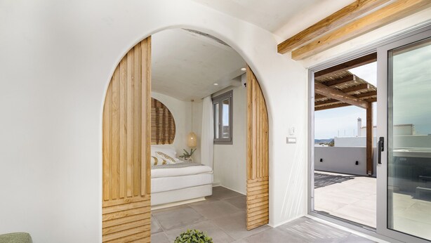Un intérieur moderne avec une arche en bois qui mène à une chambre dotée d’un lit et offrant une vue sur l’extérieur.
