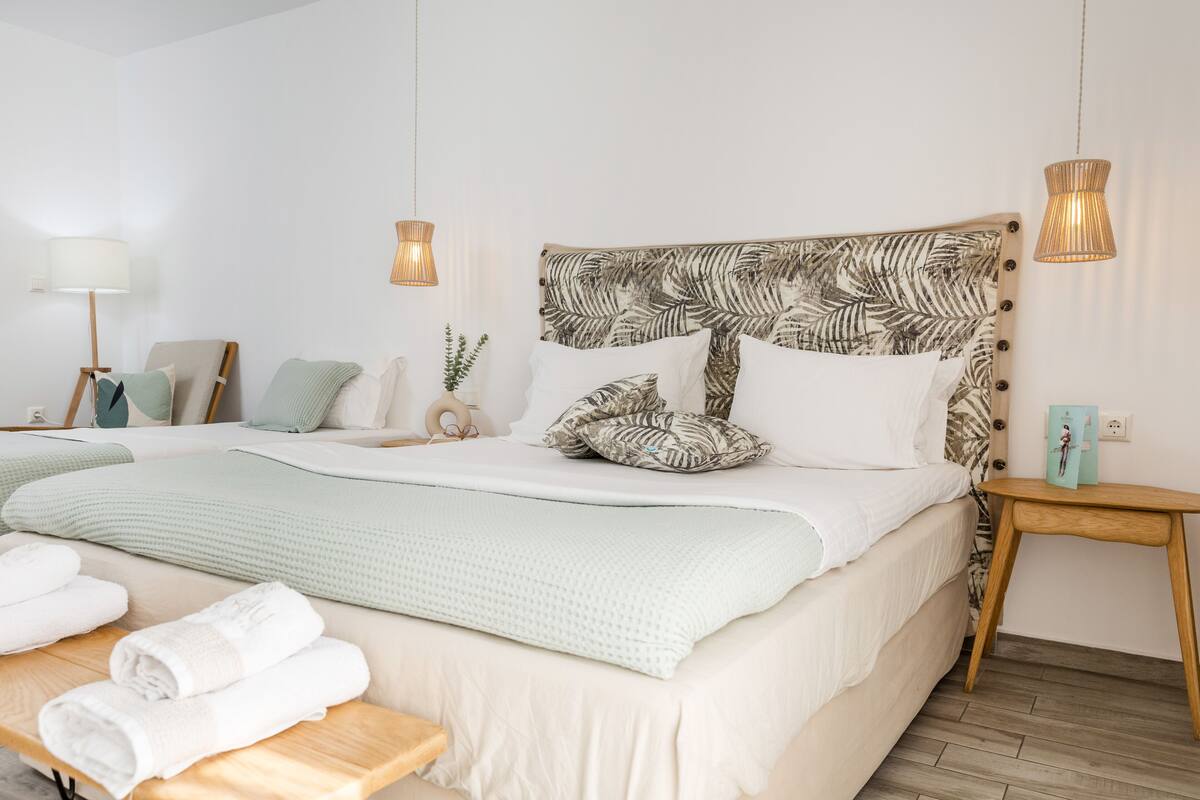 A neatly made bed with a tropical leaf-patterned headboard, a bedside table with a lamp, and a small plant.