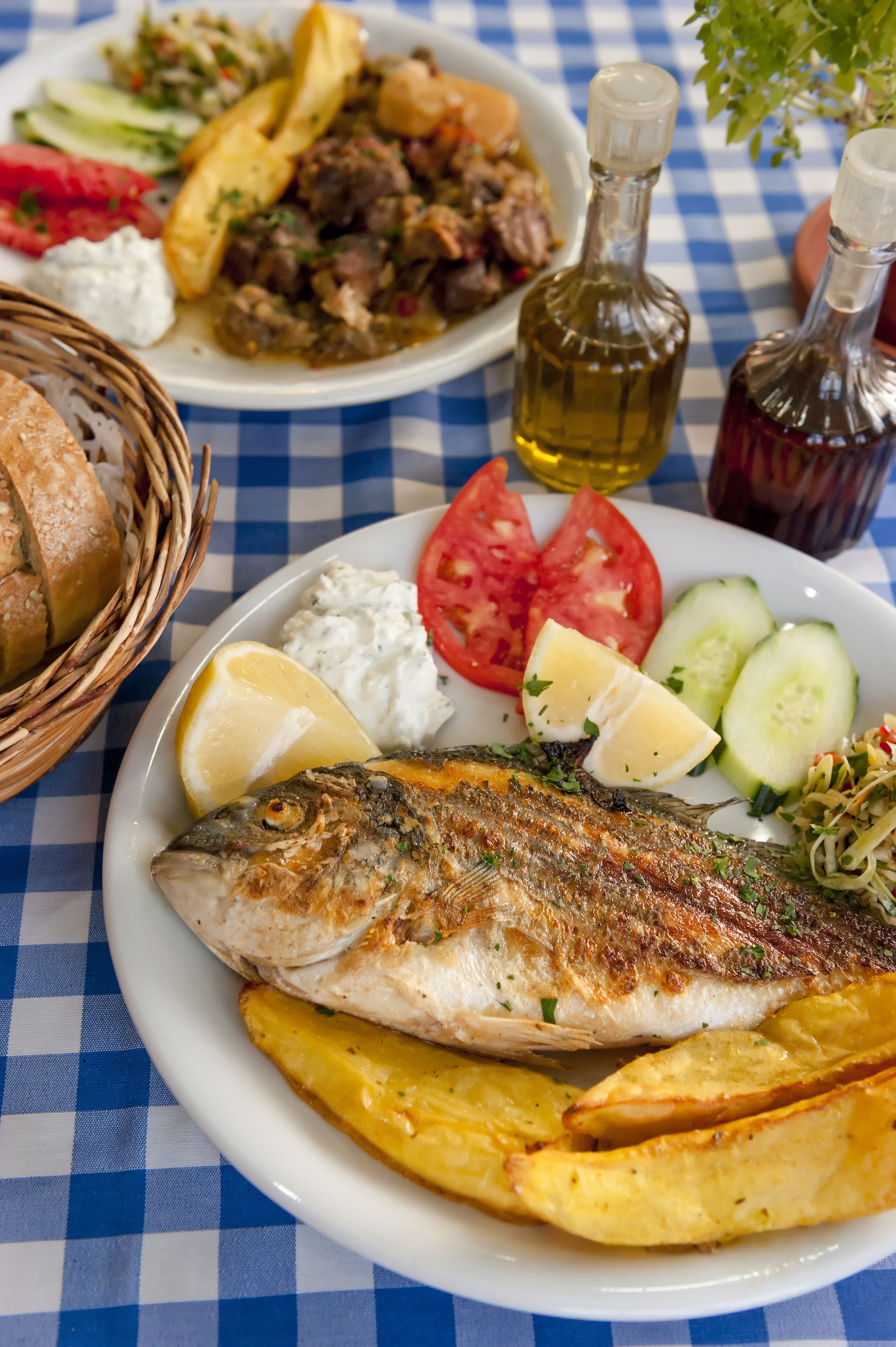 Una mesa con mantel a cuadros, un plato de pescado, rodajas de limón y guarnición de patatas.