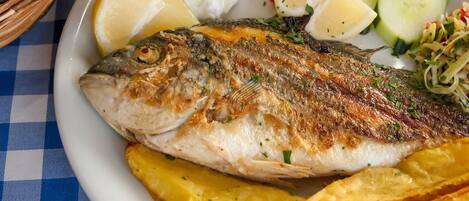 Una mesa con mantel a cuadros, un plato de pescado, rodajas de limón y guarnición de patatas.