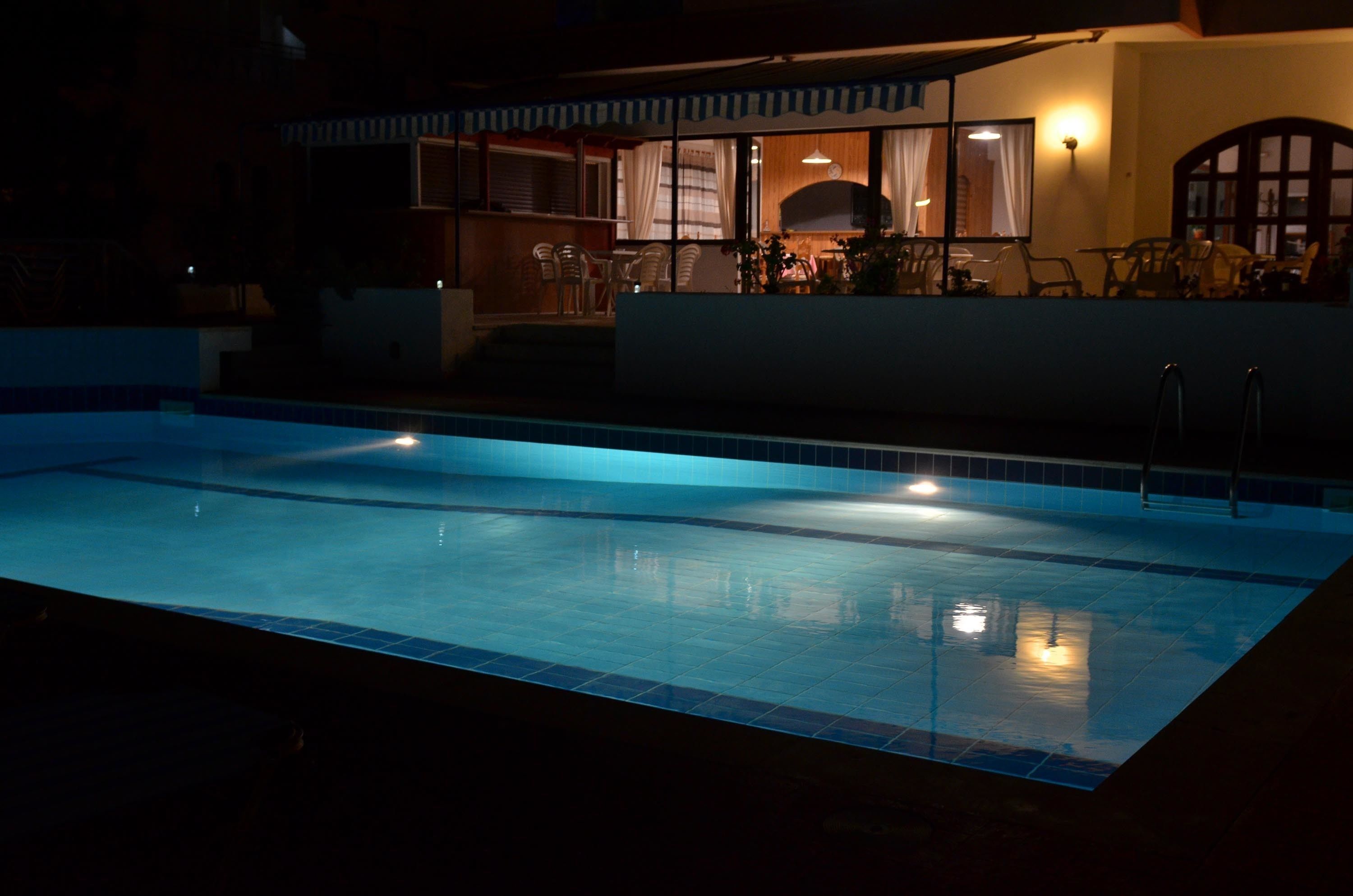 A swimming pool with a tiled edge and a small poolside area with chairs and a table.