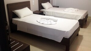 Two single beds with white linens and pillows, a wooden bench, and a small nightstand with a lamp.