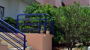 A multi-story building with a pink and white facade, outdoor stairs with blue railings, and a small tree in the foreground.