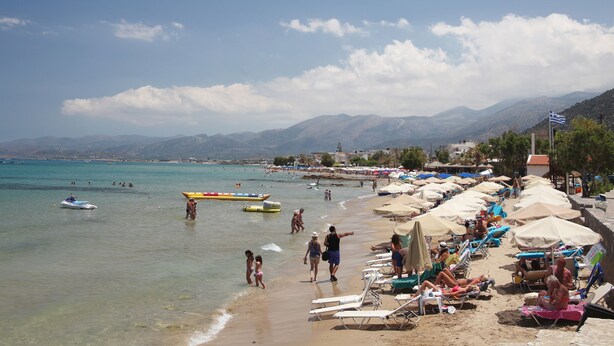 A beach with clear water, umbrellas, and people.