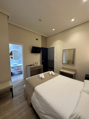 Una habitación de hotel con cama, escritorio, espejo y televisor.