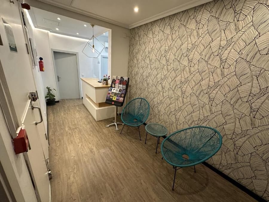 Una habitación de hotel con suelo de madera, pared estampada y dos sillas color turquesa.