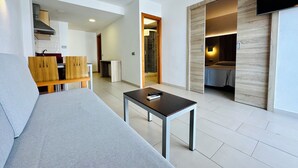 A modern living room with a sofa, a coffee table, and a TV mounted on the wall. There is a wooden cabinet and a small table in the background.