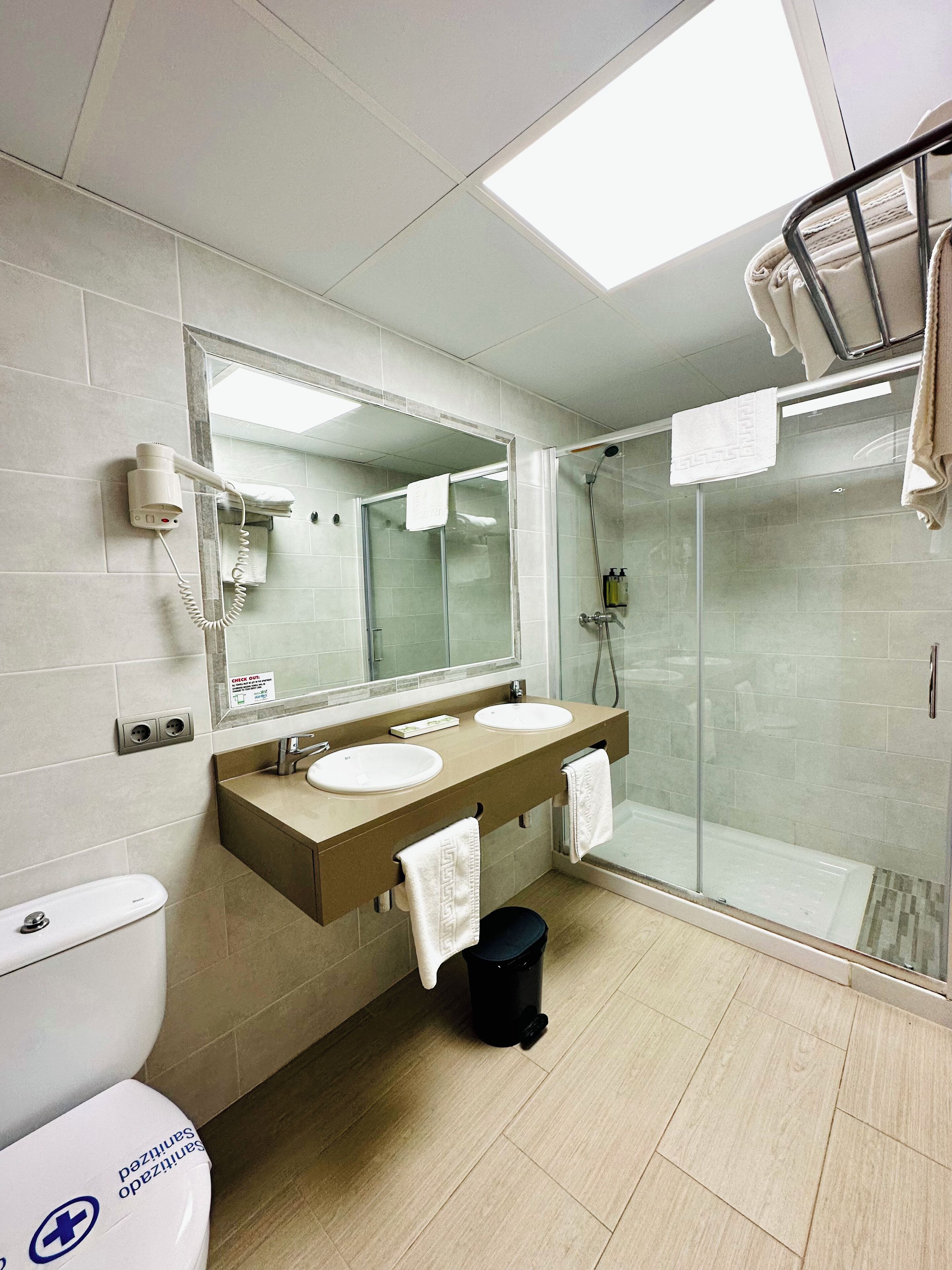 A modern bathroom with two sinks, a large mirror, a hairdryer, and a glass-enclosed shower.