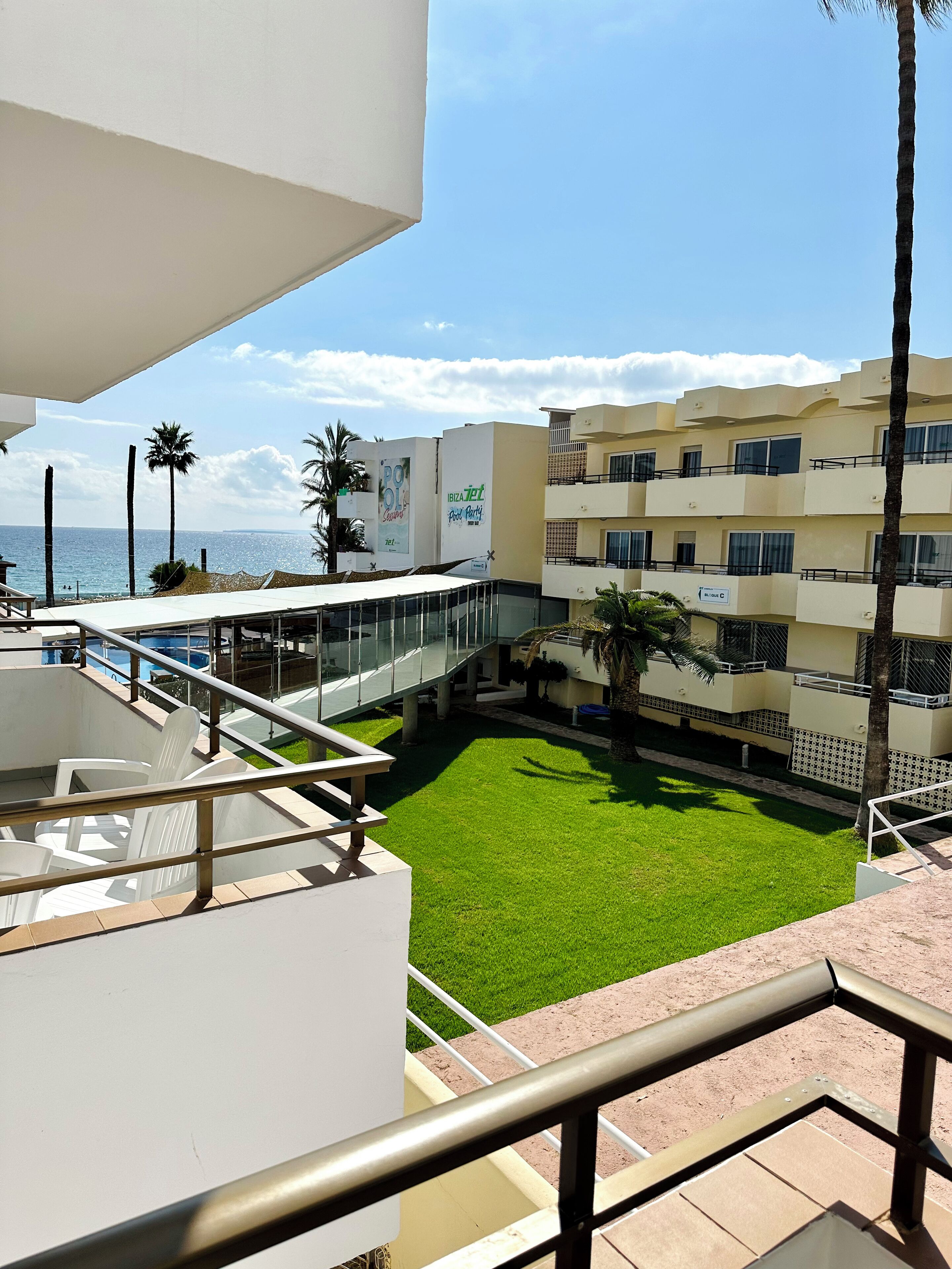 A hotel with a pool, a grassy courtyard, and a view of the sea.
