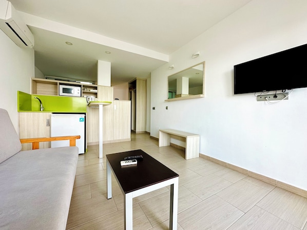 Un espacio habitable compacto con kitchenette, televisión de pantalla plana en la pared, una pequeña mesa y un banco.