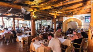 A restaurant with wooden beams, wicker furniture, and a tiled floor.