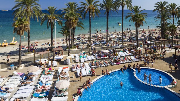 A beach resort with a large pool, sun loungers, and palm trees.
