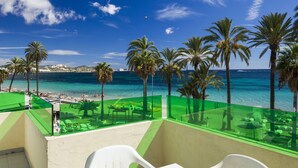 A balcony with a view of a beach, palm trees, and a clear blue sky.