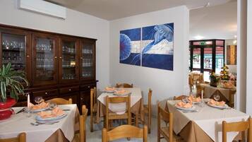 Un comedor con mesas dispuestas para cuatro, un aparador de madera con puertas de cristal y un cuadro grande en la pared.