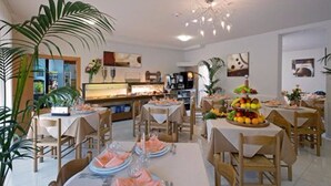 Un espace repas avec des tables dressées pour les repas, un buffet proposant divers plats et des plantes décoratives.